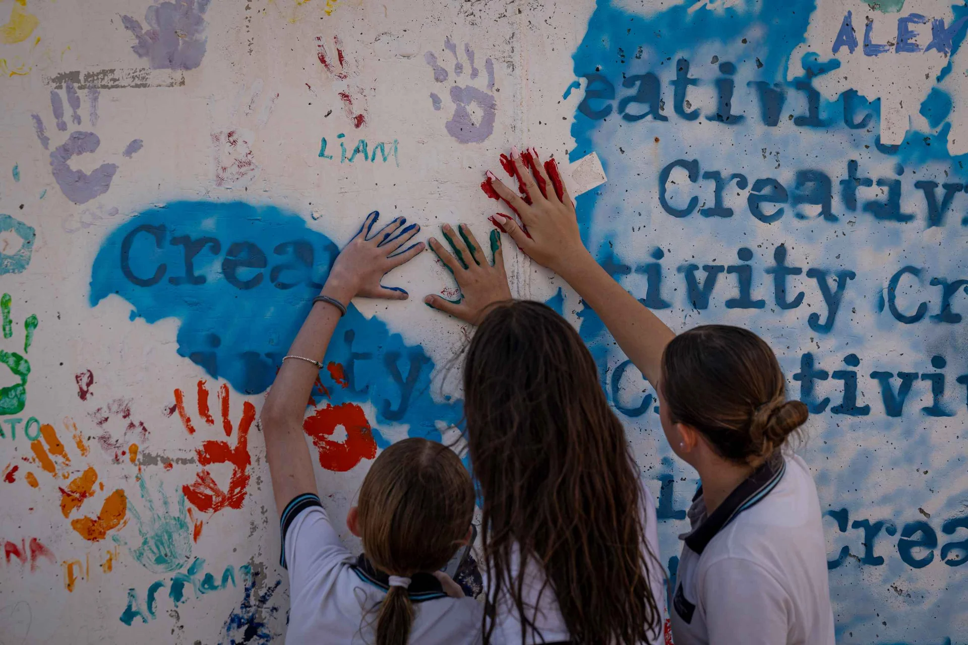 Three students painting a wall with their colorful hands 