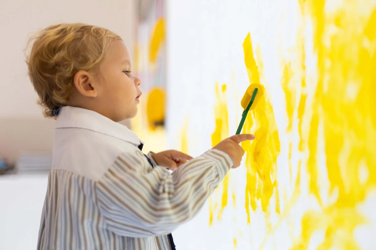 Early years child painting on a wall 