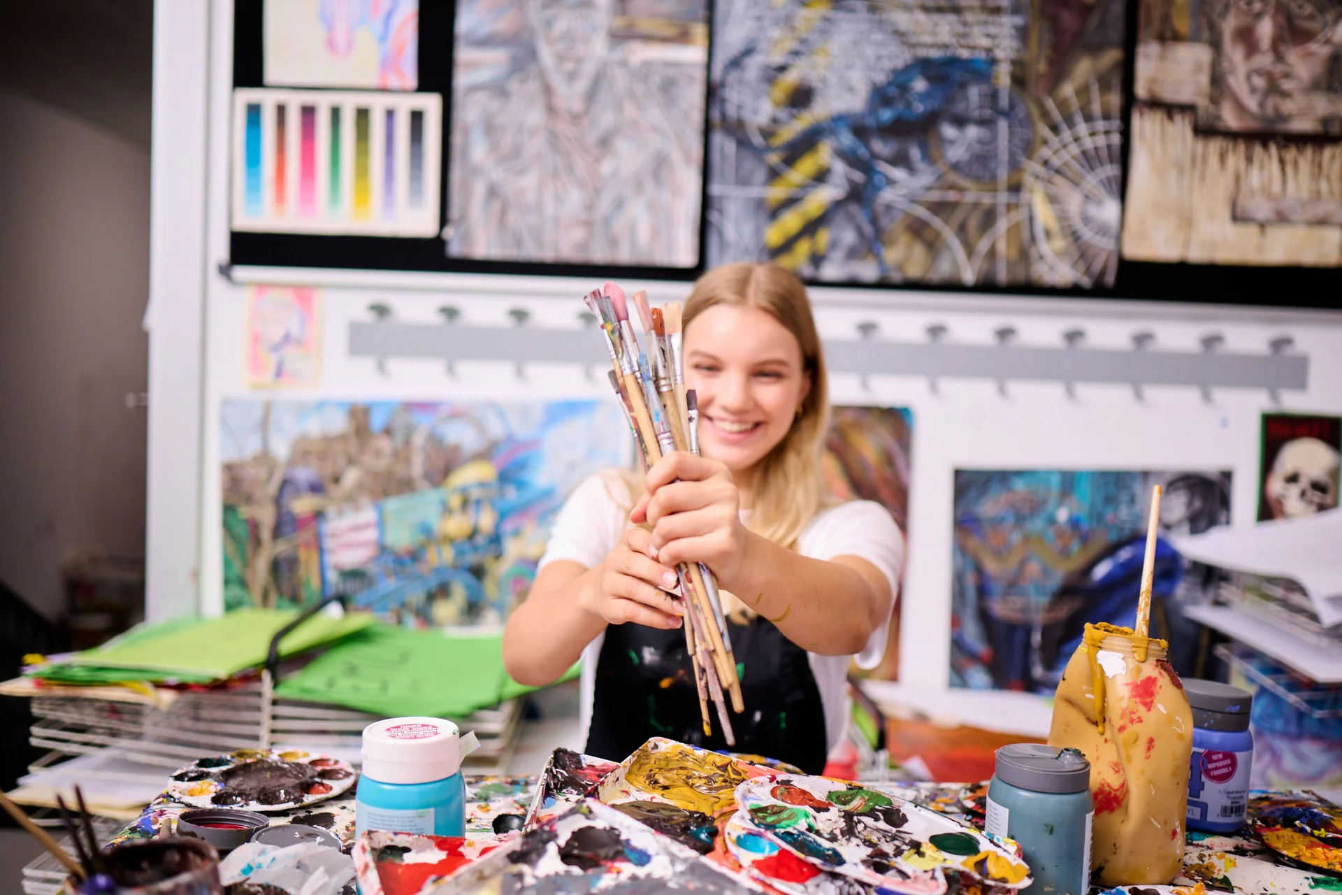 Secondary school student holding paint brushes 
